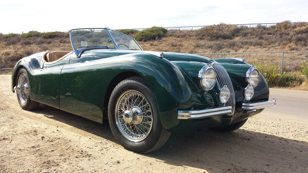 An old green sports car is parked on a dirt road.