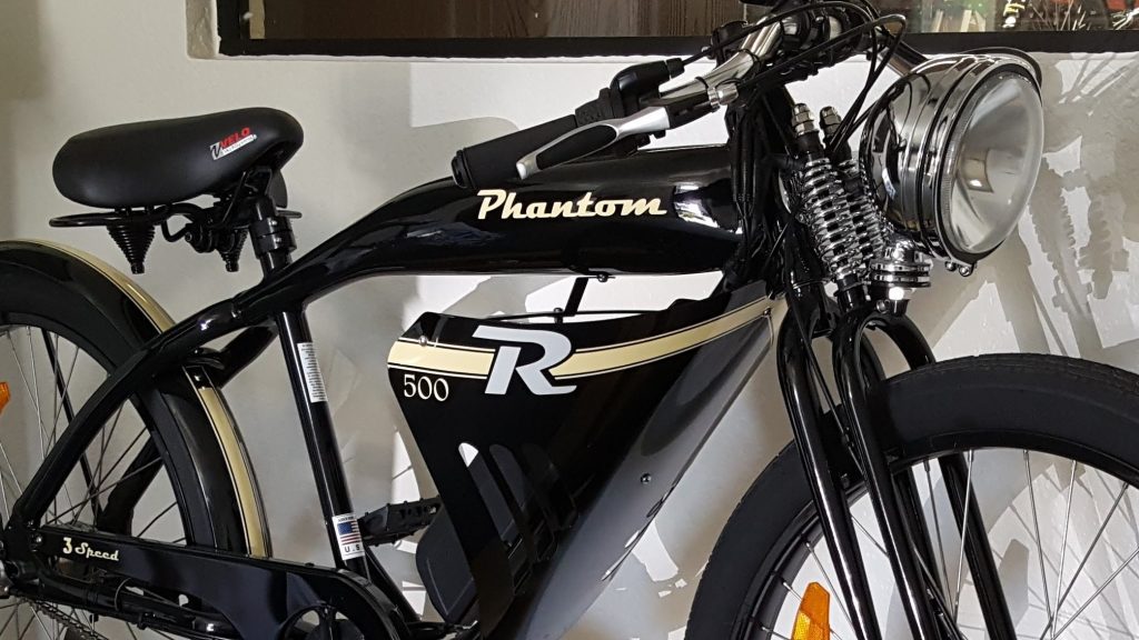 A black bike is parked in front of a white wall.