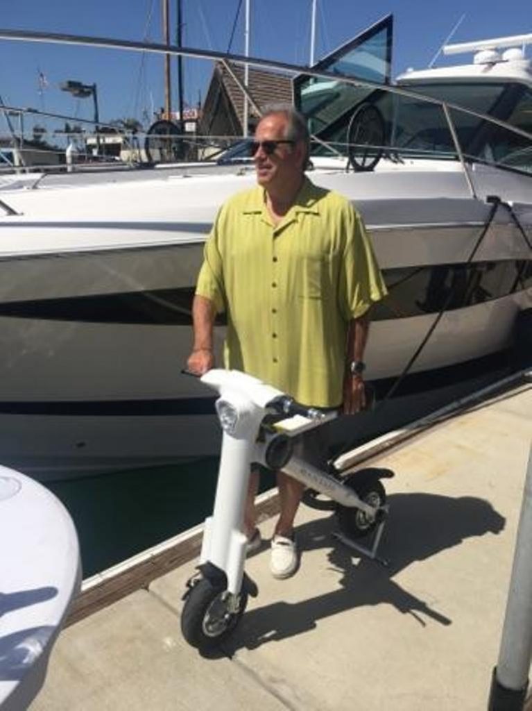 A man standing next to a boat on an electric scooter.