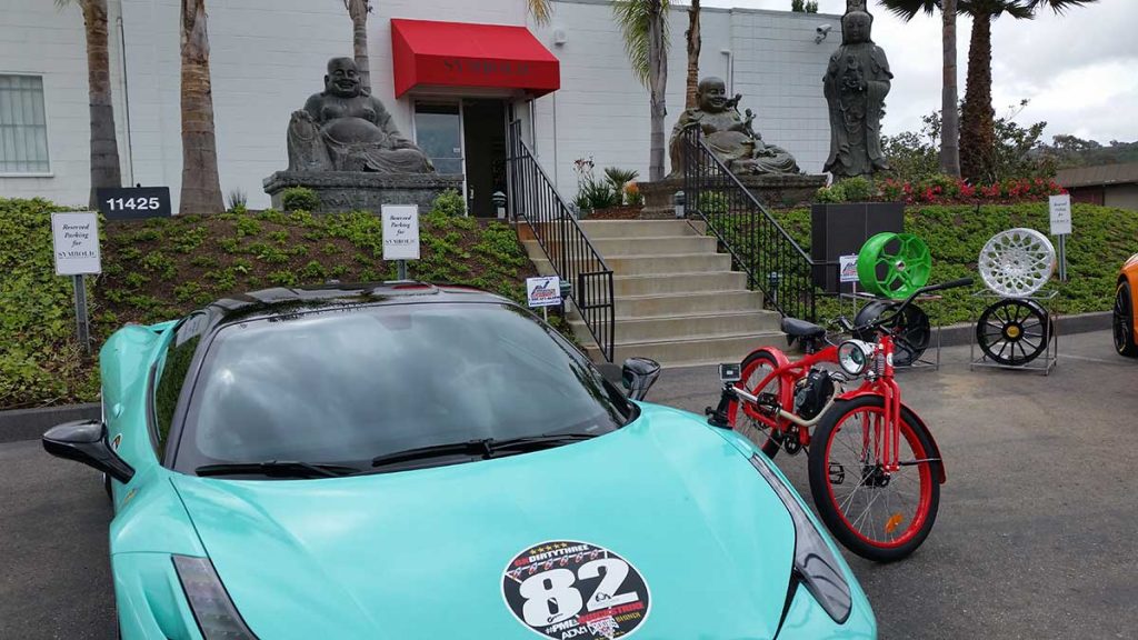 Red Phantom Shadow electric bike next to blue Lamborghini with Buddha statue in the background