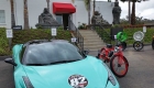 Red Phantom Shadow electric bike next to blue Lamborghini with Buddha statue in the background